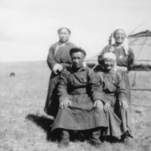 Black and white photo of a group of four Asian people sitting or standing outside a ger